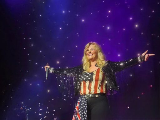 A woman in a sequined jacket and American flag-themed attire performs on stage.