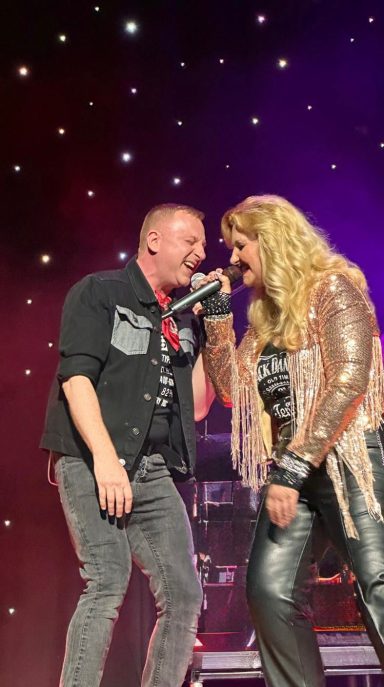 Two male performers singing closely on stage, with a starry backdrop.